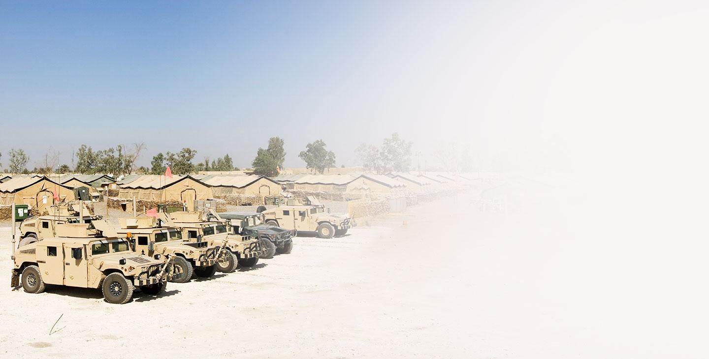 Five humvees parked in front of several army tents
